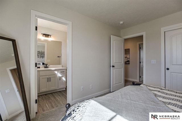 bedroom with a textured ceiling, ensuite bathroom, light colored carpet, and sink