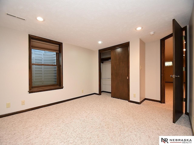 unfurnished bedroom featuring a textured ceiling, a closet, and light colored carpet