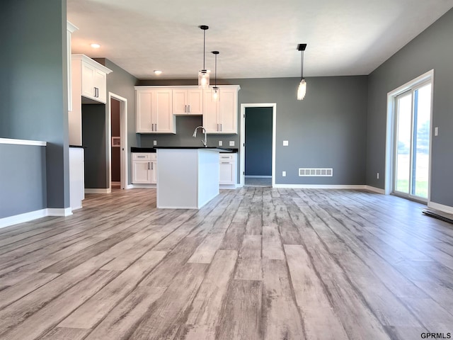 kitchen with a center island with sink, sink, hanging light fixtures, light wood-type flooring, and white cabinetry