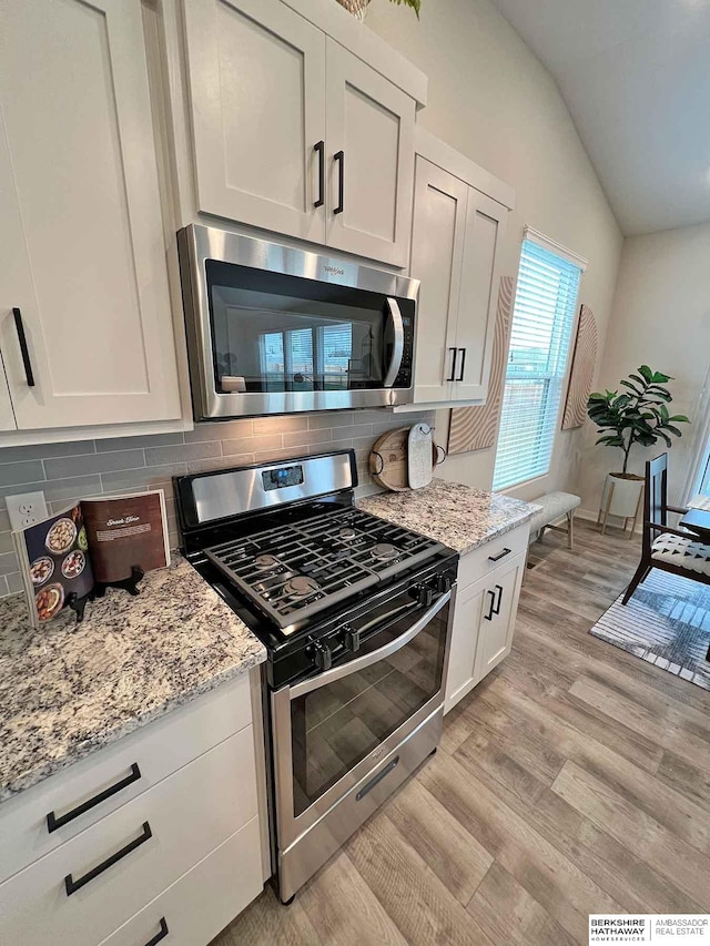 kitchen featuring backsplash, light hardwood / wood-style flooring, vaulted ceiling, appliances with stainless steel finishes, and white cabinetry