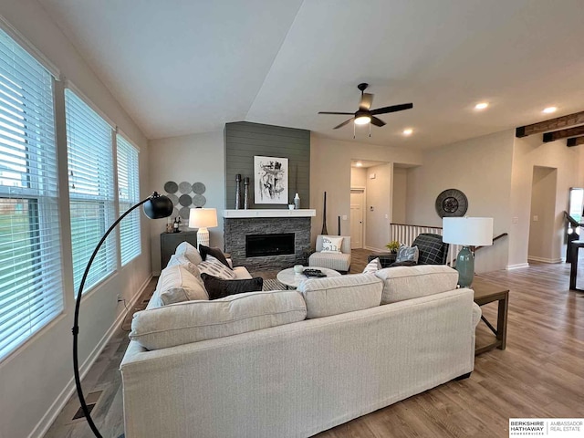 living room featuring wood-type flooring, vaulted ceiling, ceiling fan, and a stone fireplace