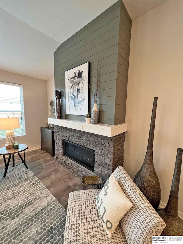 living room with a stone fireplace, wood-type flooring, and vaulted ceiling