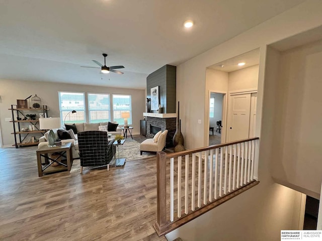 living room featuring hardwood / wood-style flooring, ceiling fan, and a stone fireplace