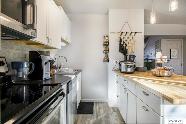 kitchen with wooden counters, decorative light fixtures, light hardwood / wood-style floors, white cabinetry, and stainless steel appliances