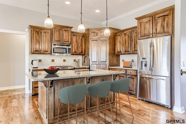 kitchen with sink, stainless steel appliances, a kitchen breakfast bar, light stone counters, and an island with sink