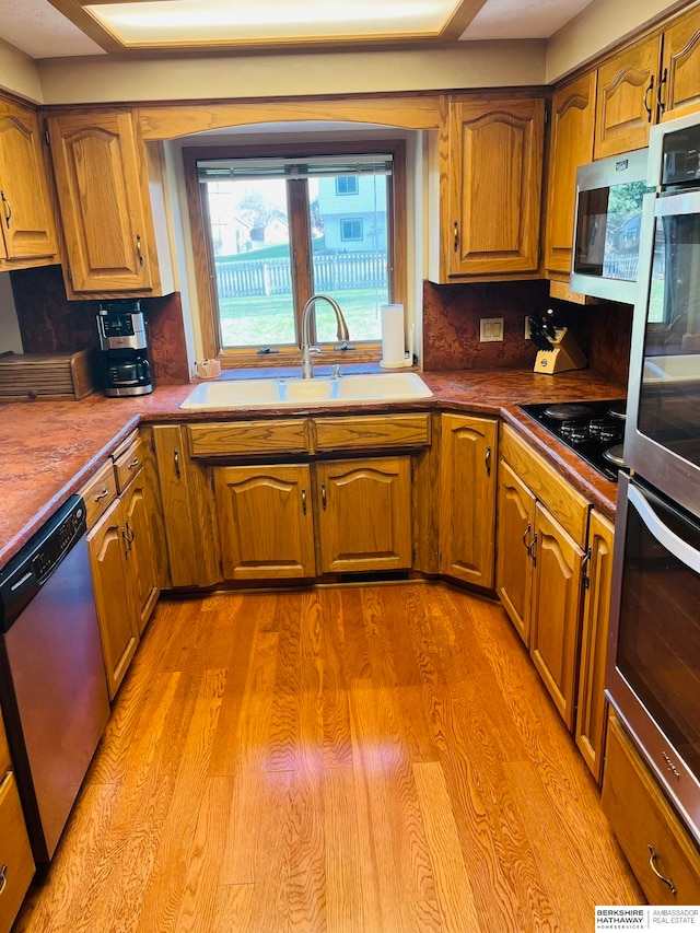 kitchen with light wood-type flooring, stainless steel appliances, backsplash, and sink