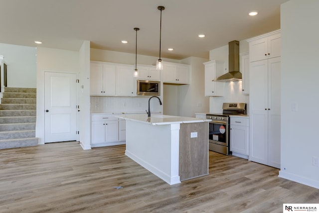 kitchen with wall chimney exhaust hood, sink, appliances with stainless steel finishes, a kitchen island with sink, and white cabinets