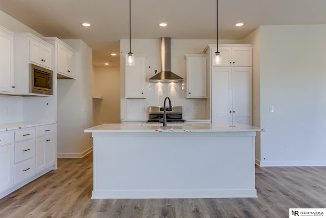 kitchen with pendant lighting, white cabinets, appliances with stainless steel finishes, and wall chimney range hood