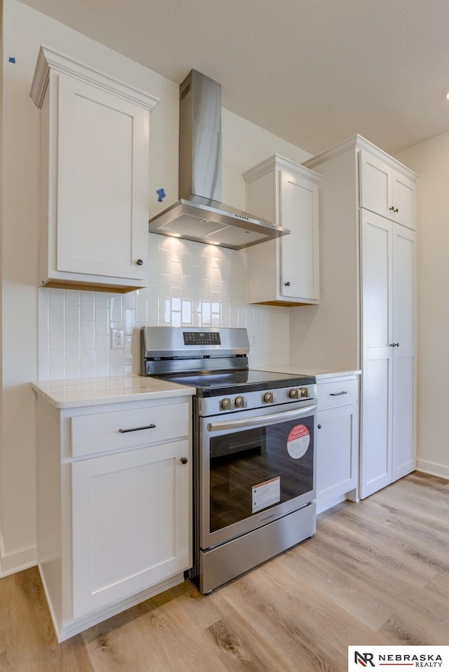 kitchen with light wood-style floors, stainless steel electric range, wall chimney exhaust hood, and light countertops