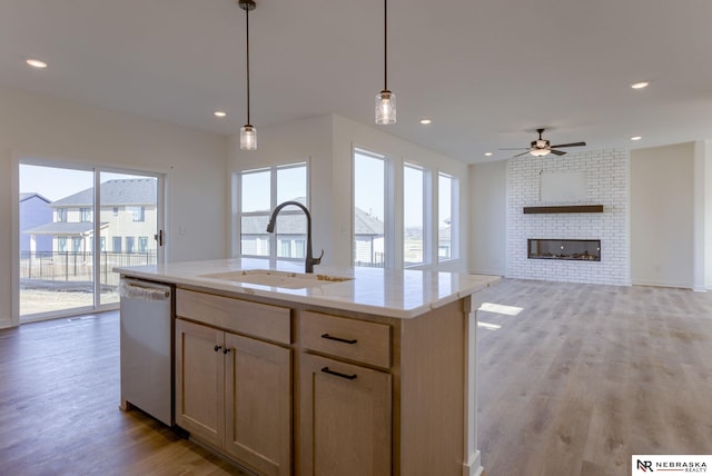 kitchen with sink, a brick fireplace, hanging light fixtures, dishwashing machine, and an island with sink