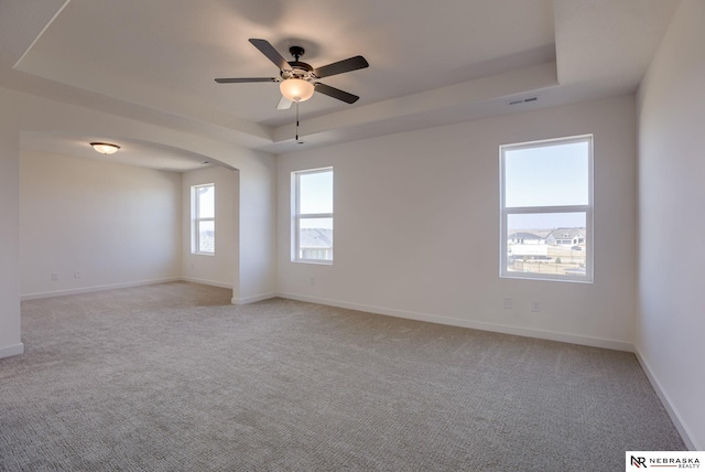 empty room with baseboards, visible vents, arched walkways, a raised ceiling, and light colored carpet