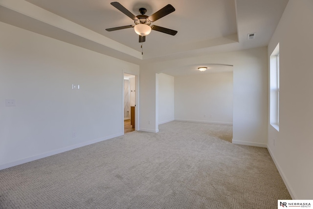 carpeted spare room with ceiling fan and a tray ceiling