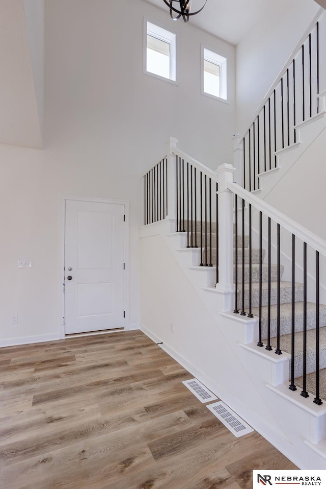 staircase featuring visible vents, wood finished floors, baseboards, and a towering ceiling