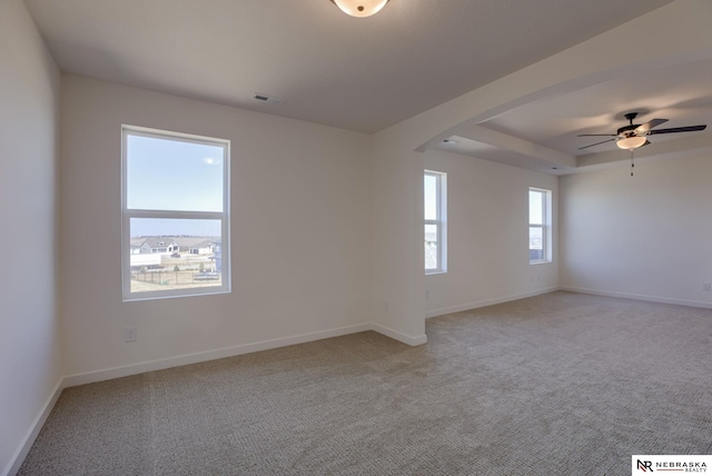 unfurnished room with visible vents, baseboards, a tray ceiling, arched walkways, and light carpet