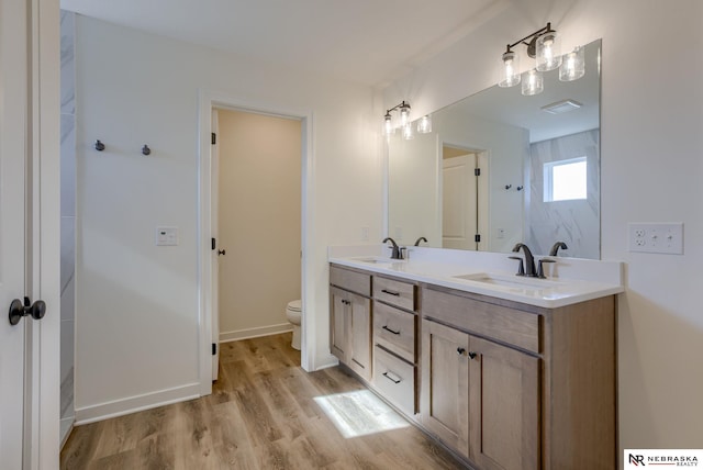 full bathroom featuring double vanity, wood finished floors, toilet, and a sink