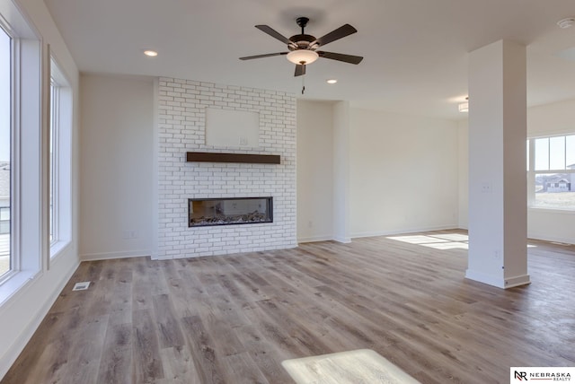 unfurnished living room featuring wood finished floors, visible vents, baseboards, ceiling fan, and a brick fireplace