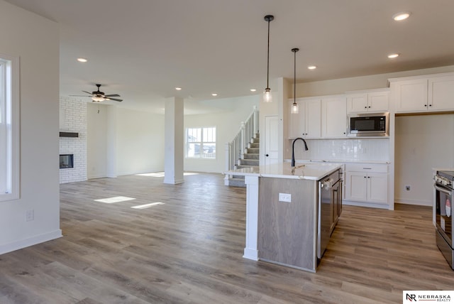 kitchen featuring pendant lighting, white cabinetry, stainless steel appliances, an island with sink, and a brick fireplace