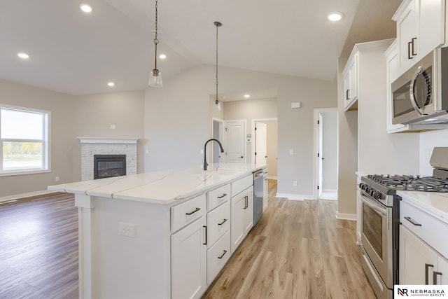 kitchen featuring pendant lighting, stainless steel appliances, white cabinets, a center island with sink, and light wood-type flooring