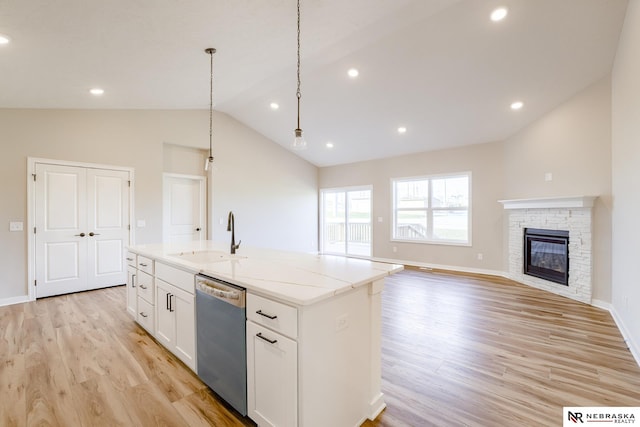 kitchen featuring stainless steel dishwasher, a kitchen island with sink, sink, and light stone countertops