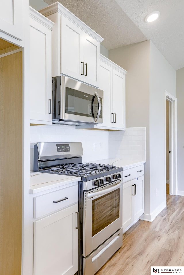 kitchen with white cabinetry, light wood-type flooring, decorative backsplash, stainless steel appliances, and a textured ceiling