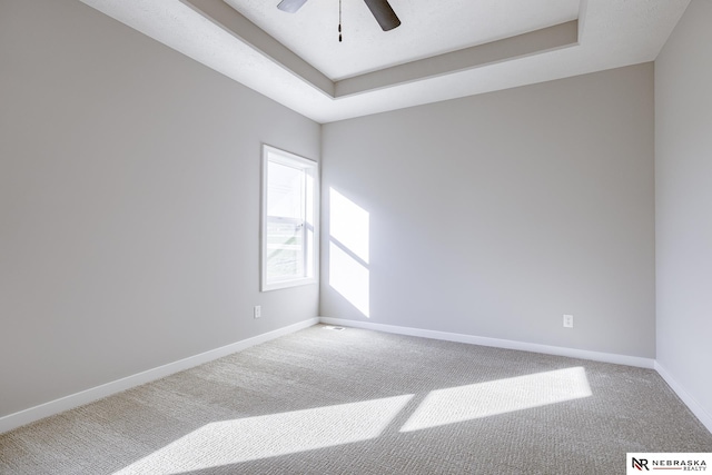 carpeted empty room with ceiling fan and a raised ceiling