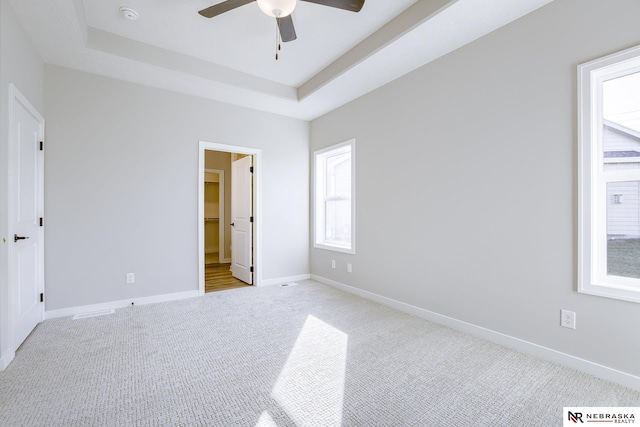 unfurnished bedroom with a tray ceiling, light colored carpet, and ceiling fan