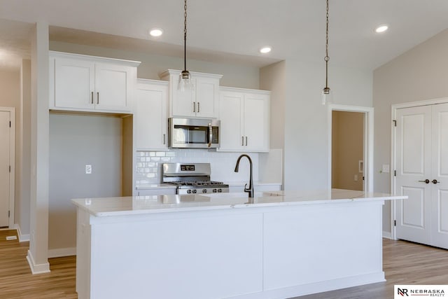 kitchen with white cabinetry, appliances with stainless steel finishes, decorative light fixtures, and a kitchen island with sink