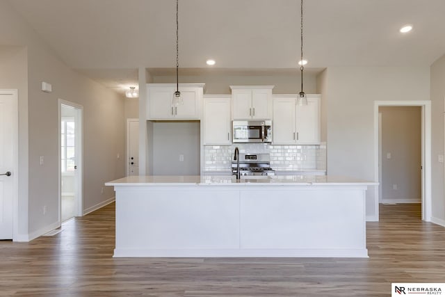 kitchen featuring appliances with stainless steel finishes, decorative light fixtures, an island with sink, and white cabinets