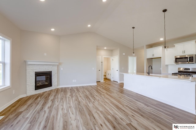 unfurnished living room featuring lofted ceiling, sink, a stone fireplace, and light wood-type flooring