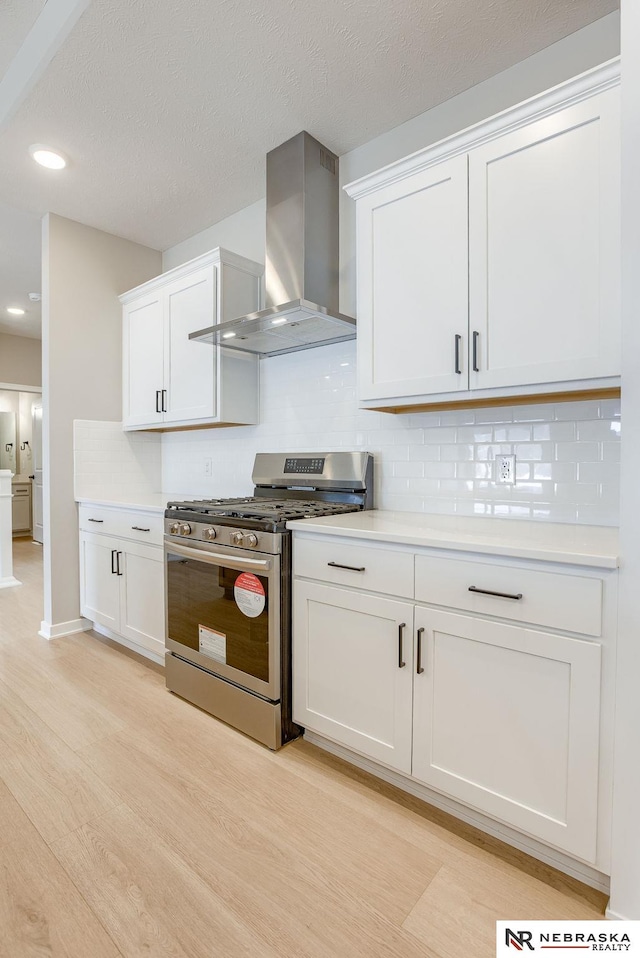 kitchen with light countertops, stainless steel gas stove, light wood-style flooring, and wall chimney exhaust hood