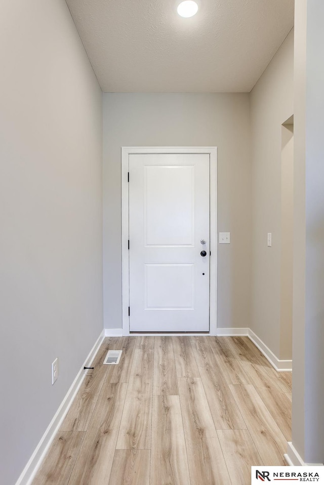 doorway with a textured ceiling and light wood-type flooring