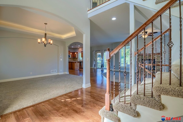 foyer with carpet flooring, a tray ceiling, and ceiling fan with notable chandelier