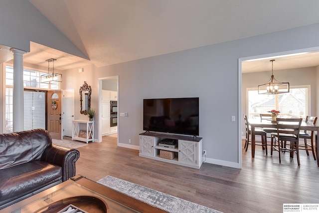 living room featuring a notable chandelier, decorative columns, wood-type flooring, and vaulted ceiling