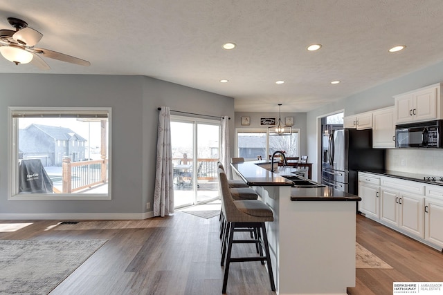 kitchen with white cabinetry, sink, an island with sink, decorative light fixtures, and a breakfast bar area