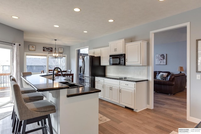 kitchen featuring sink, black appliances, white cabinets, light hardwood / wood-style floors, and hanging light fixtures