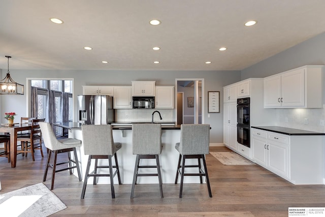 kitchen with backsplash, black appliances, pendant lighting, light hardwood / wood-style flooring, and white cabinetry