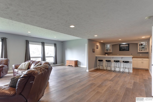 living room featuring a textured ceiling, light hardwood / wood-style floors, and indoor bar