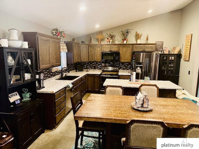 kitchen featuring sink, stainless steel refrigerator with ice dispenser, a center island with sink, decorative backsplash, and range with two ovens