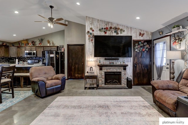 living room featuring vaulted ceiling, a stone fireplace, and ceiling fan