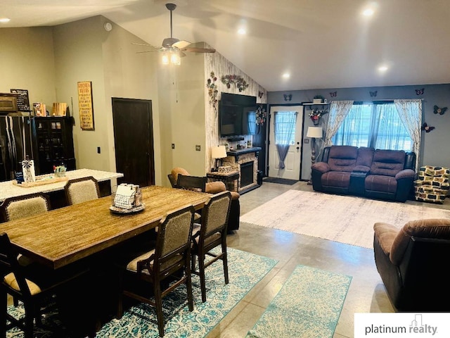 dining room with ceiling fan, a fireplace, and vaulted ceiling