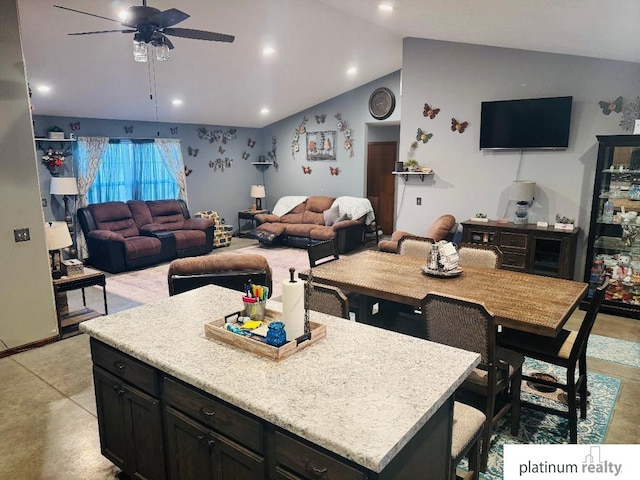 kitchen featuring a breakfast bar area, ceiling fan, light stone counters, a kitchen island, and vaulted ceiling