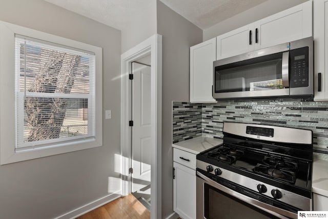 kitchen featuring decorative backsplash, a textured ceiling, stainless steel appliances, and white cabinetry