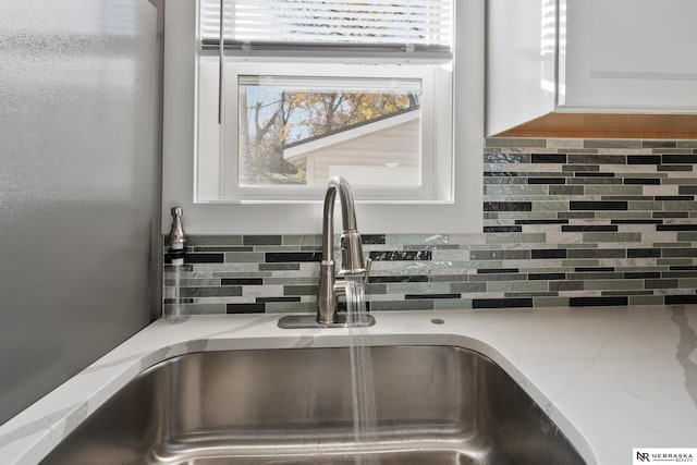 details featuring decorative backsplash, sink, white cabinets, and light stone counters