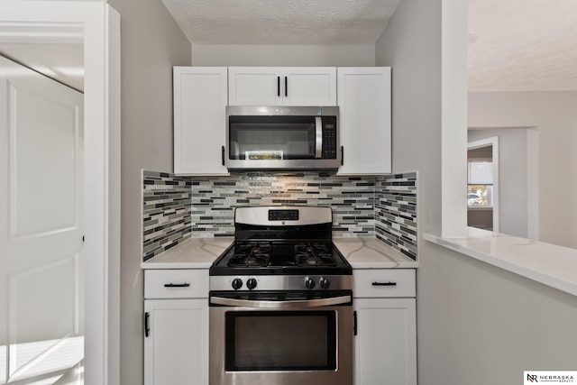 kitchen featuring white cabinetry, light stone countertops, a textured ceiling, decorative backsplash, and appliances with stainless steel finishes