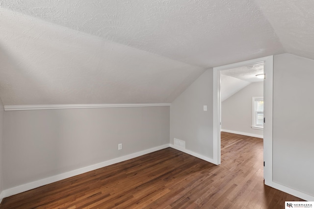 bonus room featuring vaulted ceiling, dark wood-type flooring, and a textured ceiling