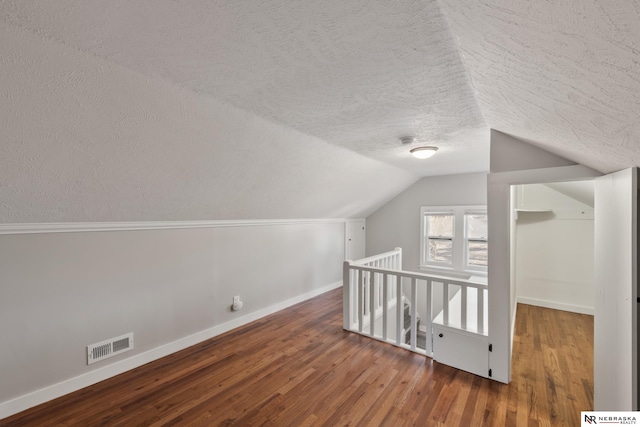 bonus room with wood-type flooring, a textured ceiling, and vaulted ceiling