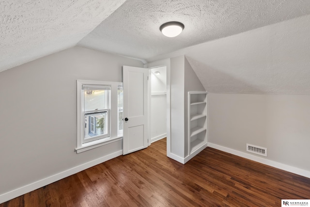 additional living space featuring dark hardwood / wood-style flooring, lofted ceiling, and a textured ceiling