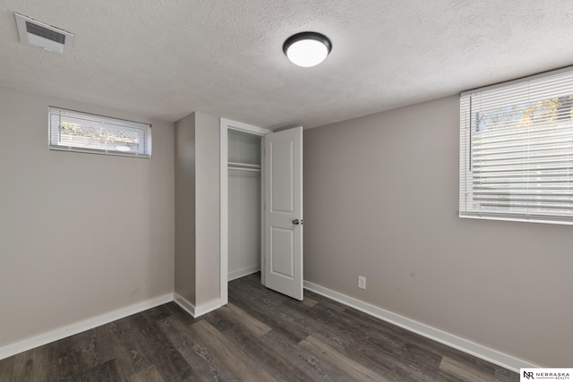 unfurnished bedroom with a textured ceiling, dark hardwood / wood-style floors, and a closet