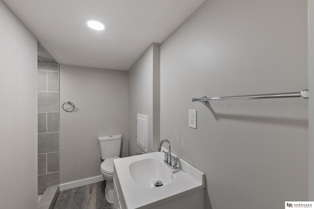 bathroom with tiled shower, hardwood / wood-style floors, vanity, and toilet