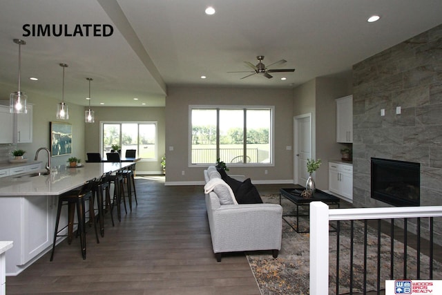 living room with a tiled fireplace, ceiling fan, sink, and dark wood-type flooring